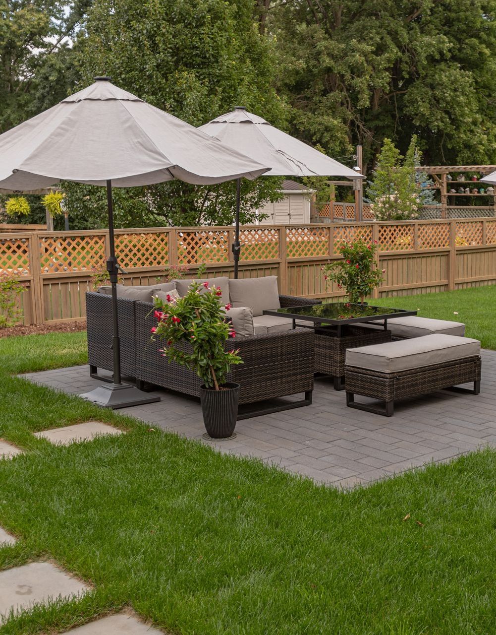 Patio furniture with umbrellas on a paved area, green lawn, wooden fence in the background.
