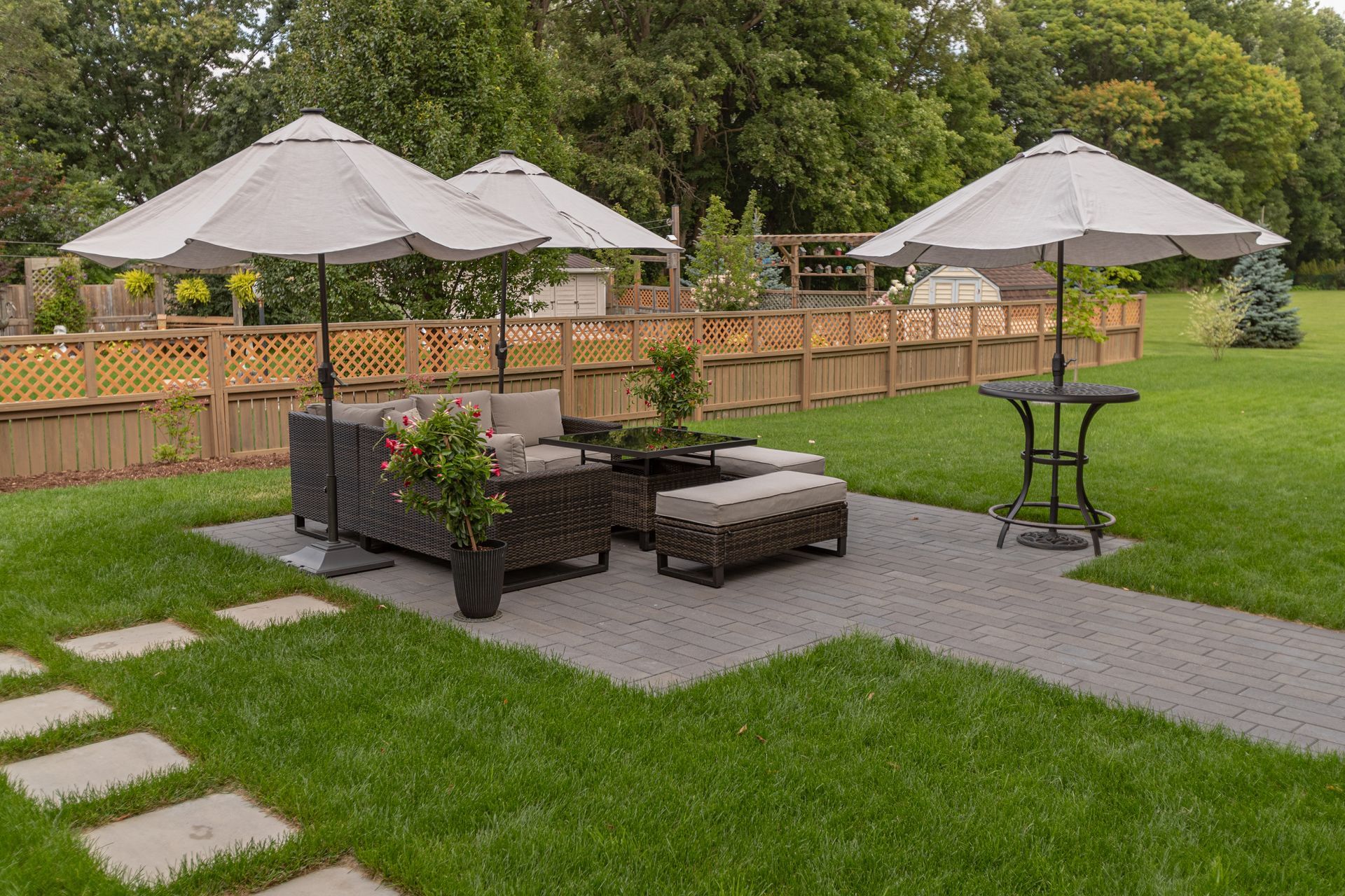 Patio with outdoor furniture, umbrellas, and stone pathway in a backyard.