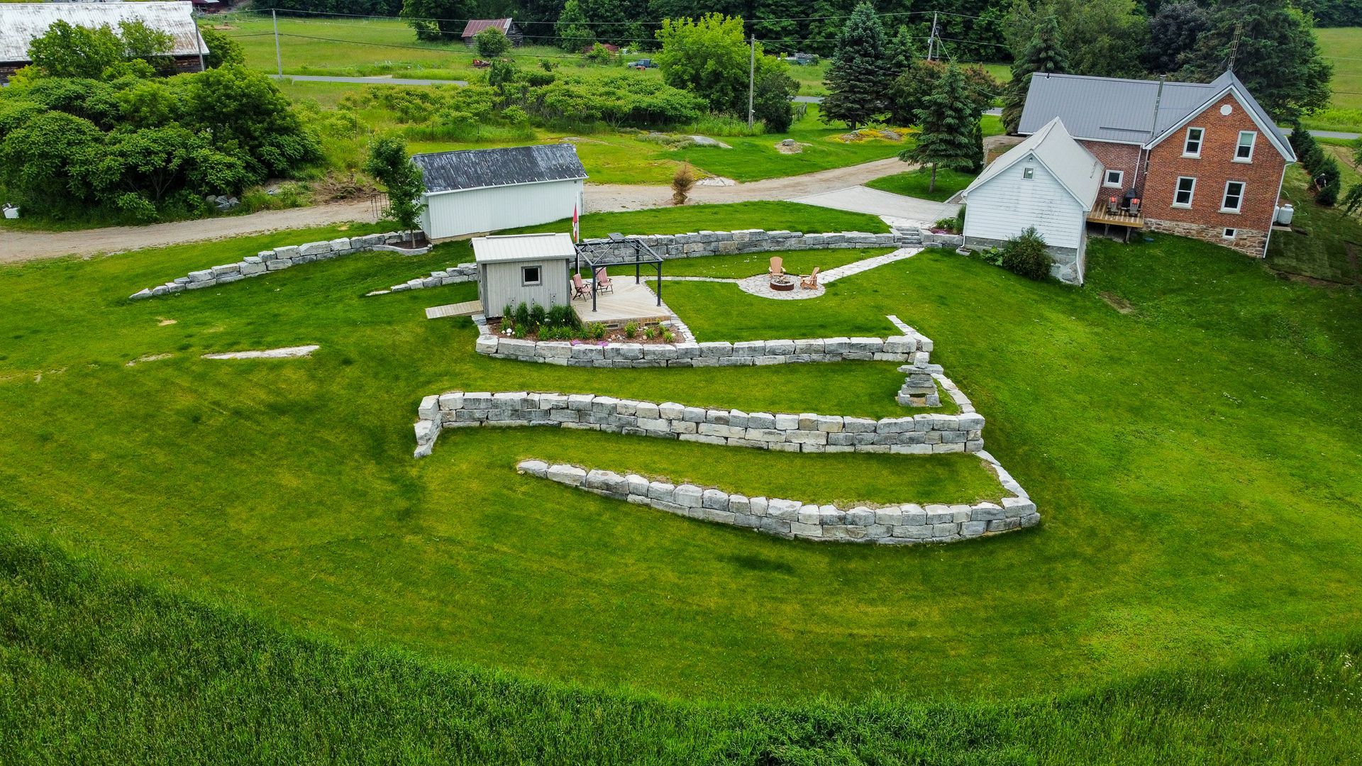Aerial view of a green hillside with stone retaining walls, small buildings, and a farmhouse in the background.
