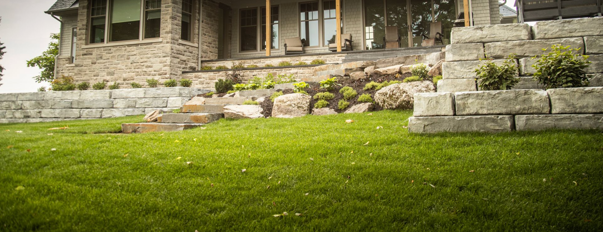 Front yard with terraced stone retaining walls, structured planting beds, and a manicured lawn.