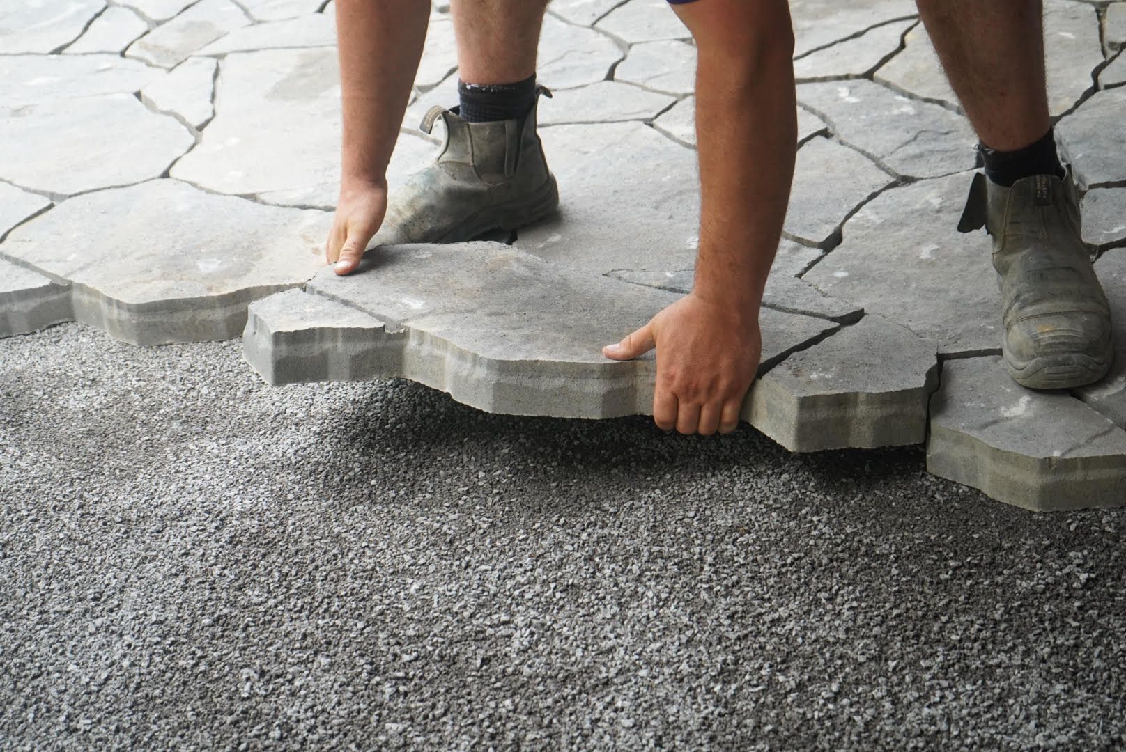 Worker installing interlock pavers over compacted gravel base during hardscaping project in Kingston