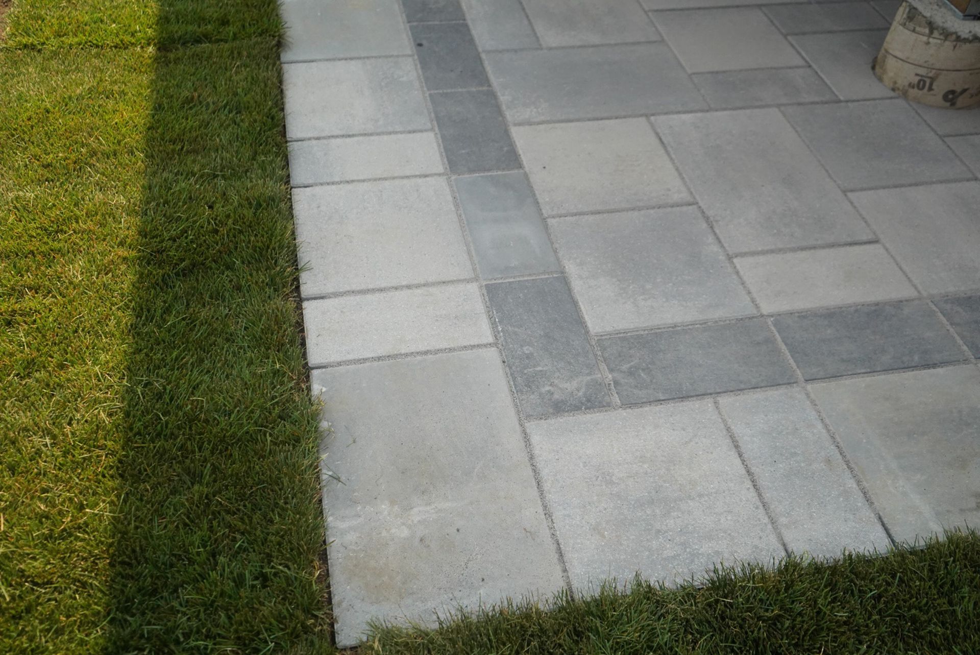 Paved patio with gray rectangular stones, bordered by green grass.