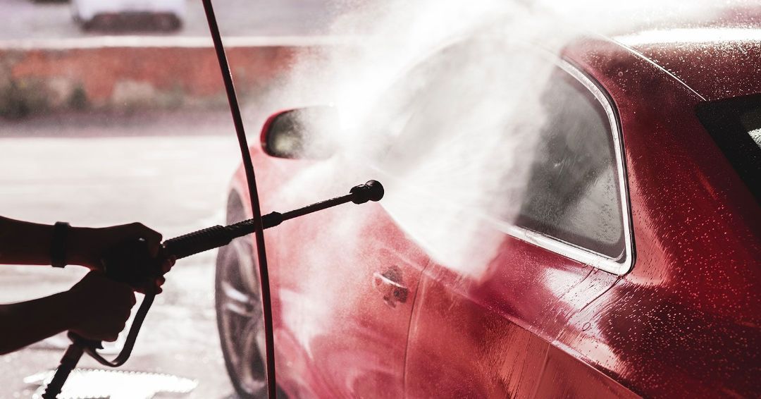 a person is washing a red car with a high pressure washer .