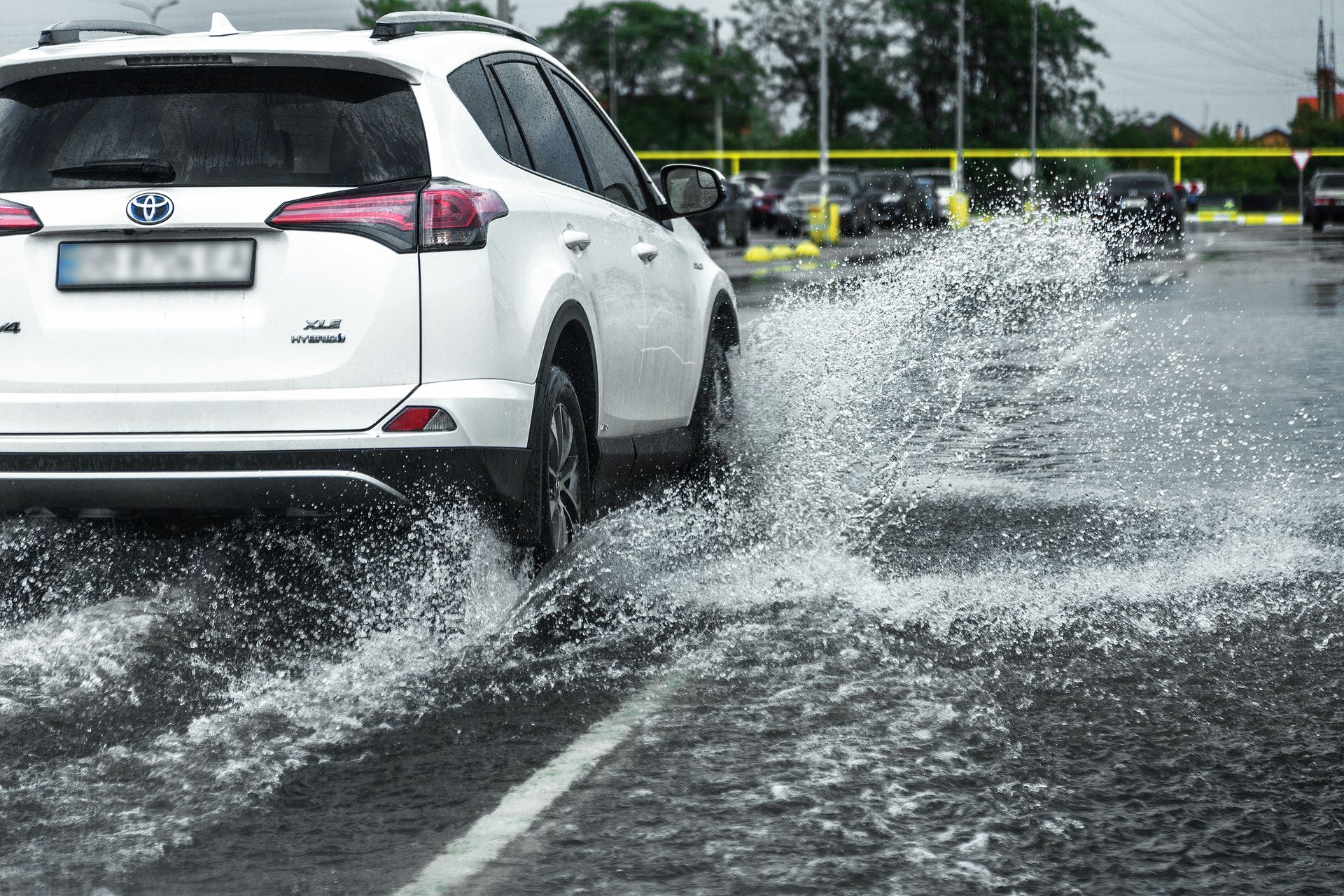 A white car is driving through a flooded parking lot.