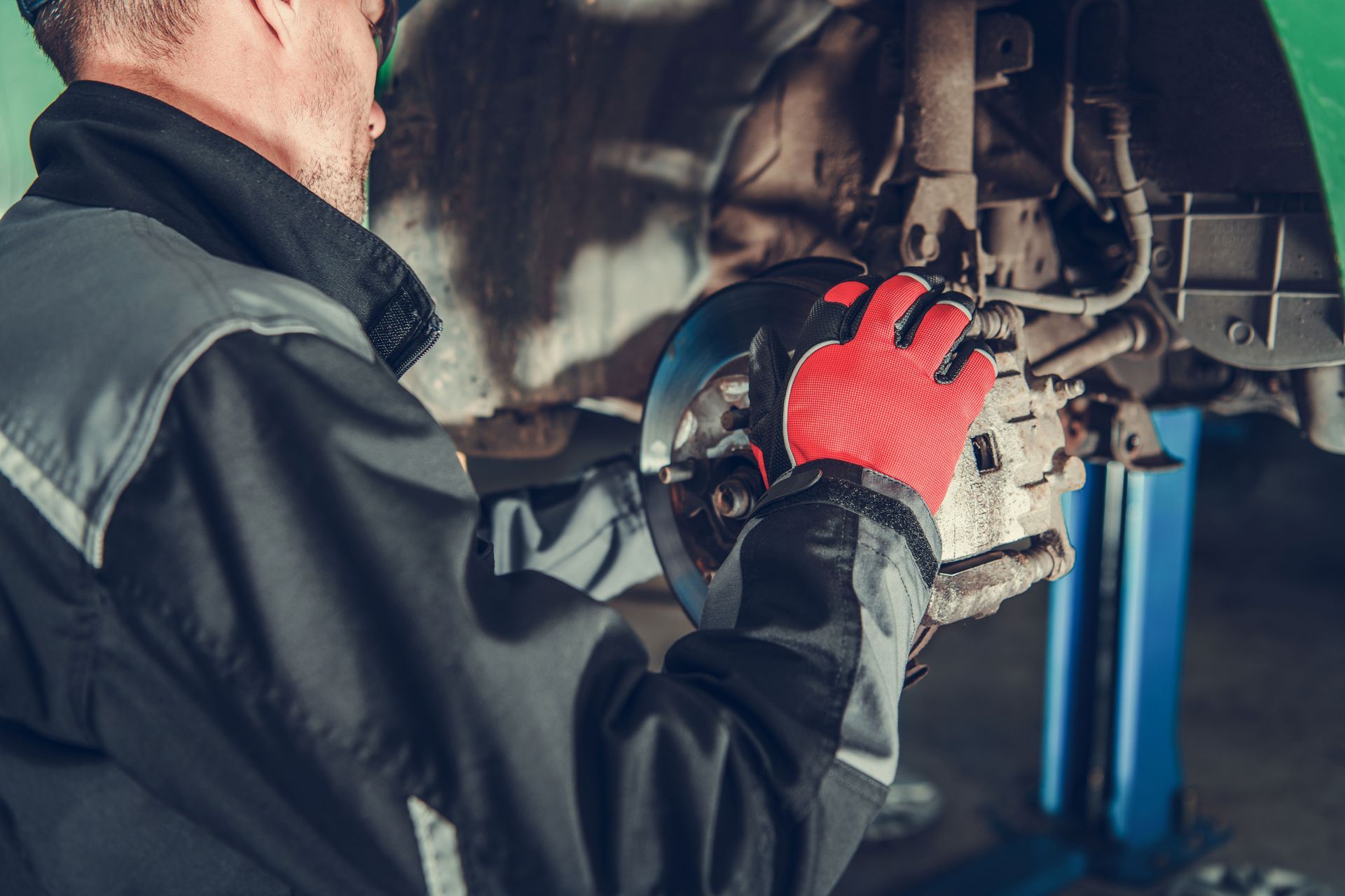 a man wearing red gloves is working on a car on a lift .