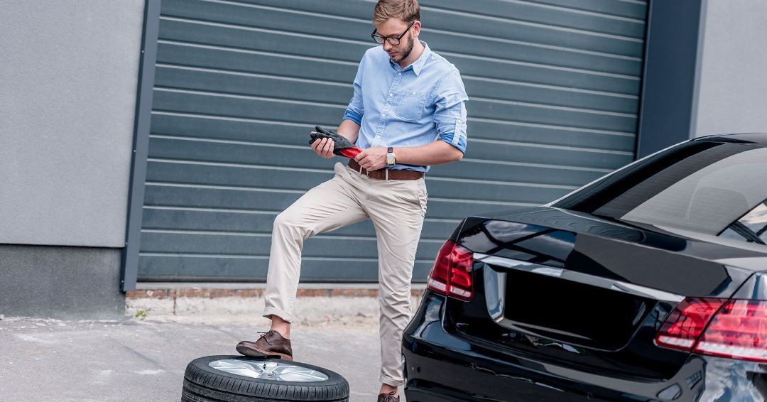 a man is standing on a tire next to a car .