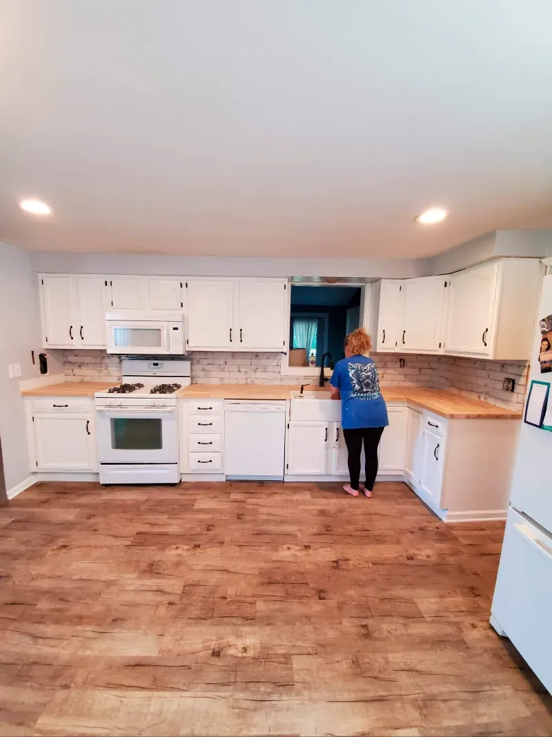 A woman in a blue shirt is standing in a kitchen.