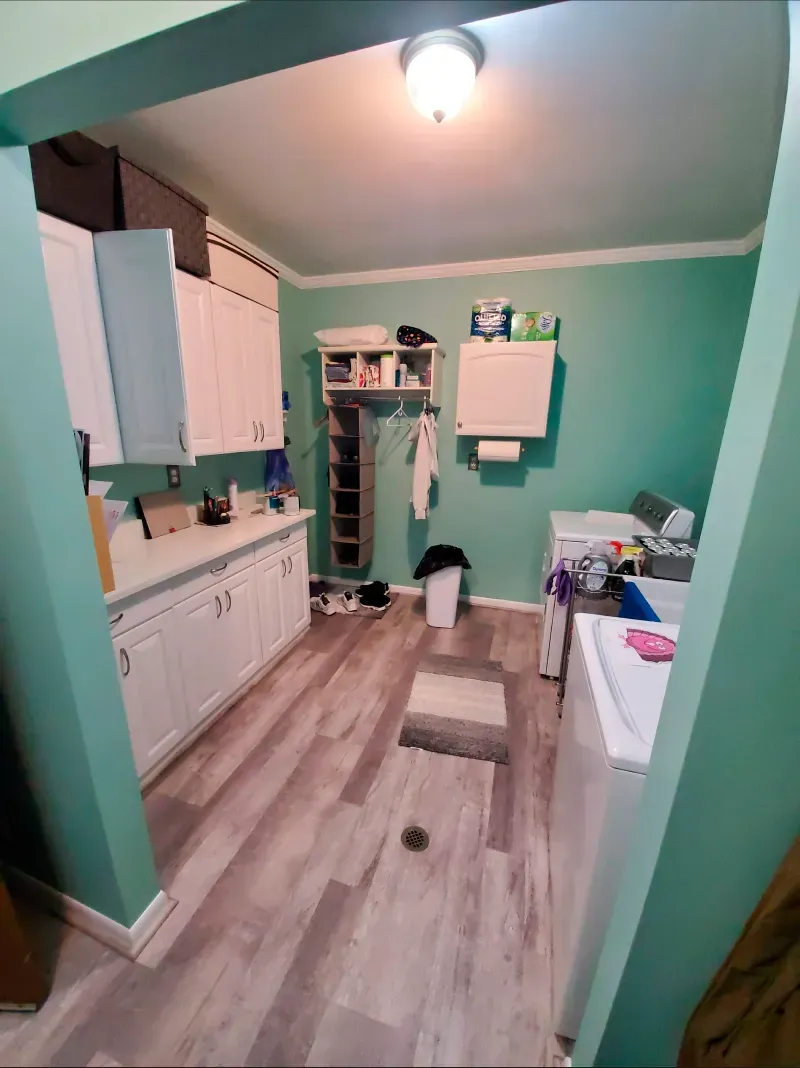 A laundry room with green walls , white cabinets , a washer and dryer , and a refrigerator.