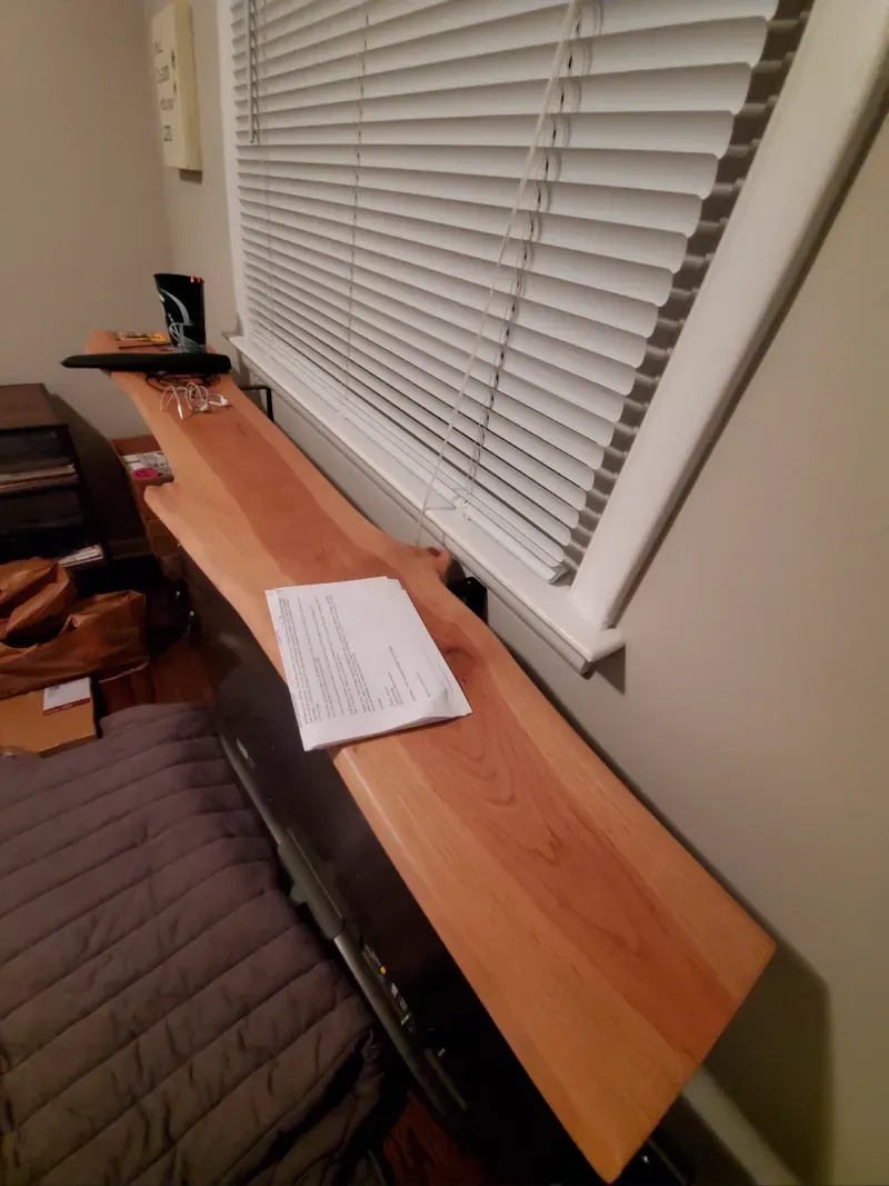 A wooden shelf sits in front of a window with blinds