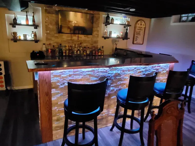 A bar with stools and bottles on it in a basement.