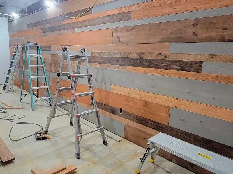 Two ladders are sitting in front of a wooden wall.