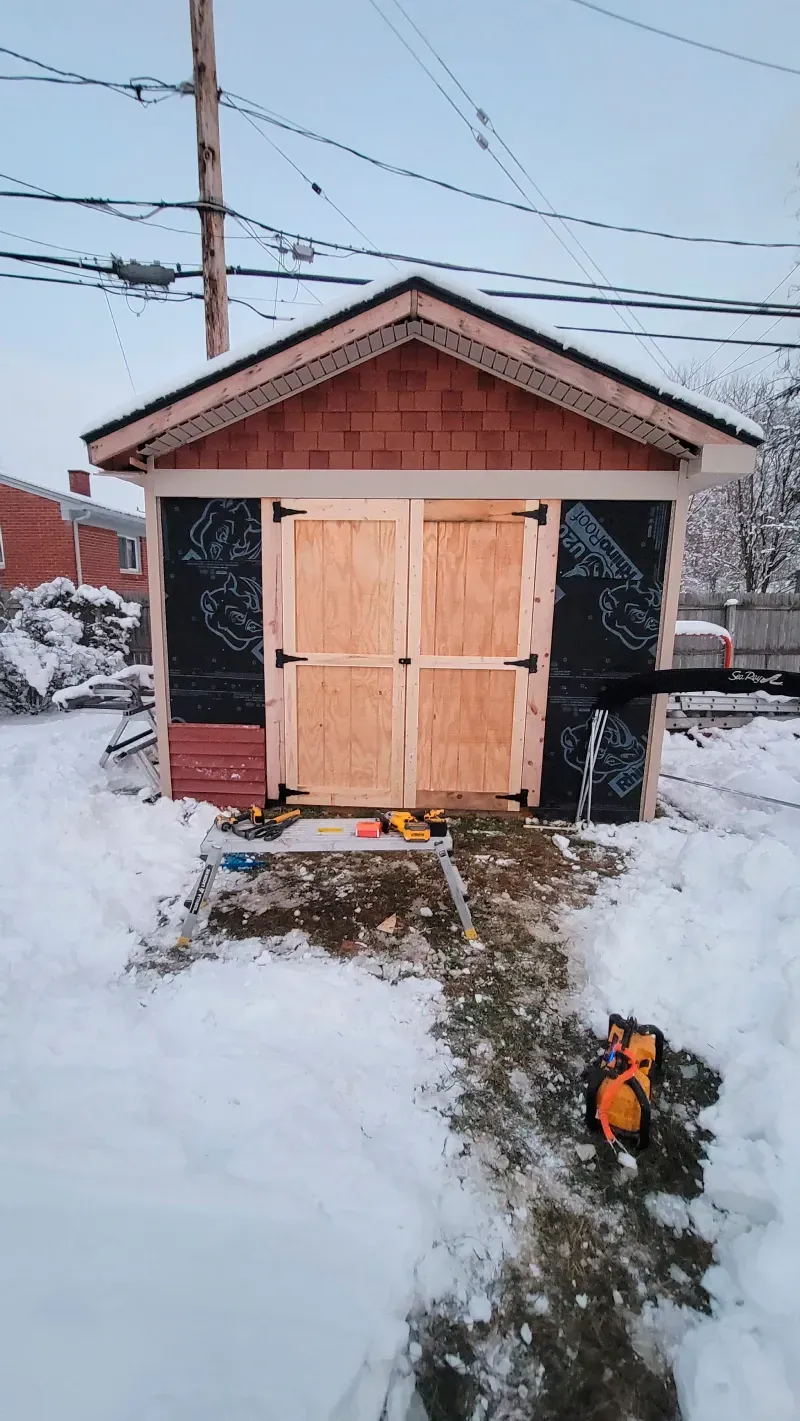 A small shed is sitting in the middle of a snowy yard.