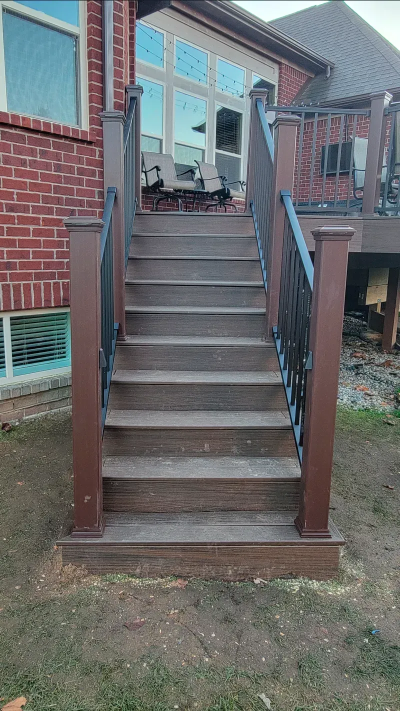 A wooden deck with stairs leading up to a brick house.