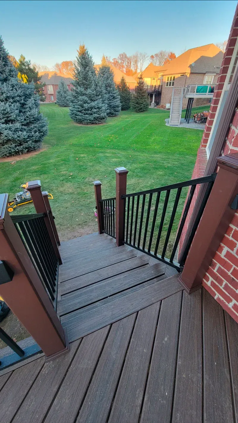 A wooden deck with stairs leading up to a lush green yard.