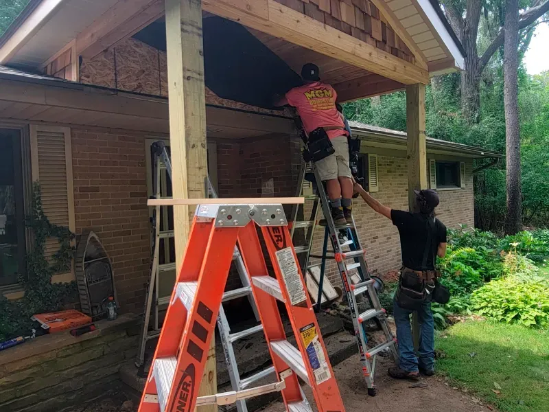 Two men are working on a porch with ladders.