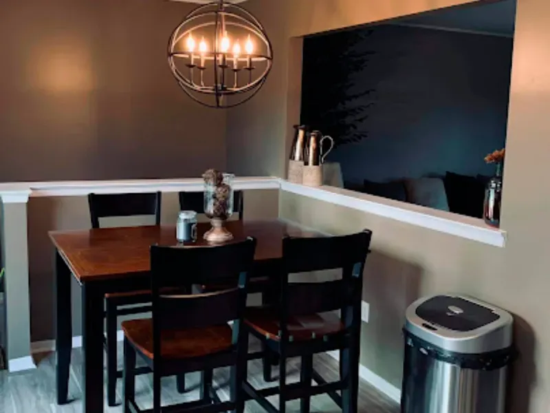 A dining room with a table and chairs and a trash can.