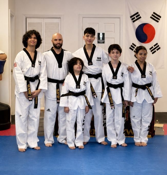Two children in black and white martial arts uniforms practice a chokehold on a mat. One child smiles.