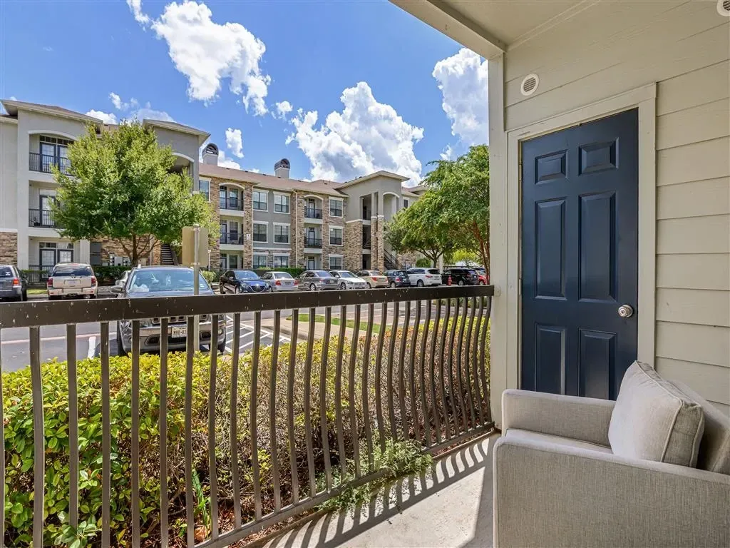 View of apartment buildings from a balcony, showing a parked car and a blue door.