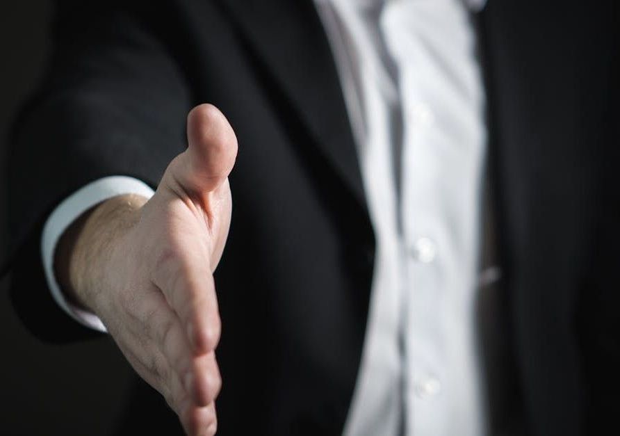 A man in a suit is reaching out his hand to shake someone's hand.