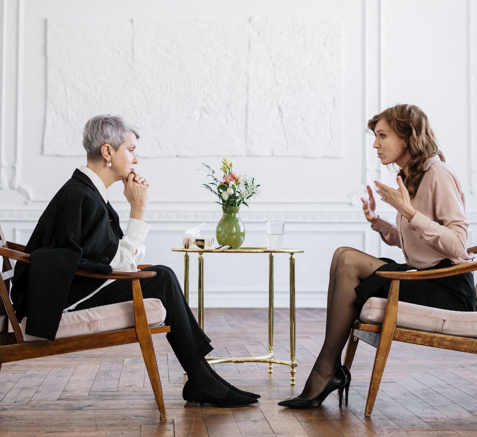 Two women are sitting in chairs talking to each other.