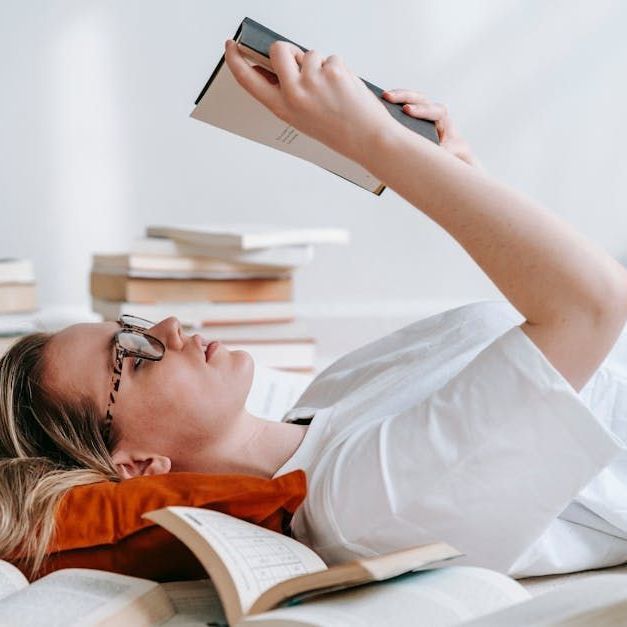 A woman wearing glasses is laying on a bed reading a book