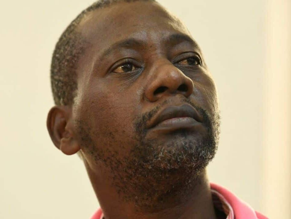 A man with a beard is wearing a pink shirt and looking up.