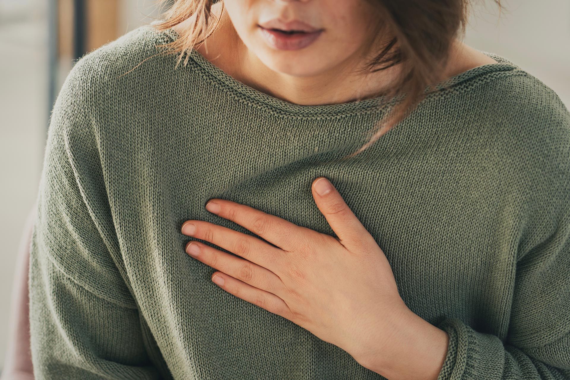 Person in a green sweater holding a hand to their chest, showing a close-up of discomfort.