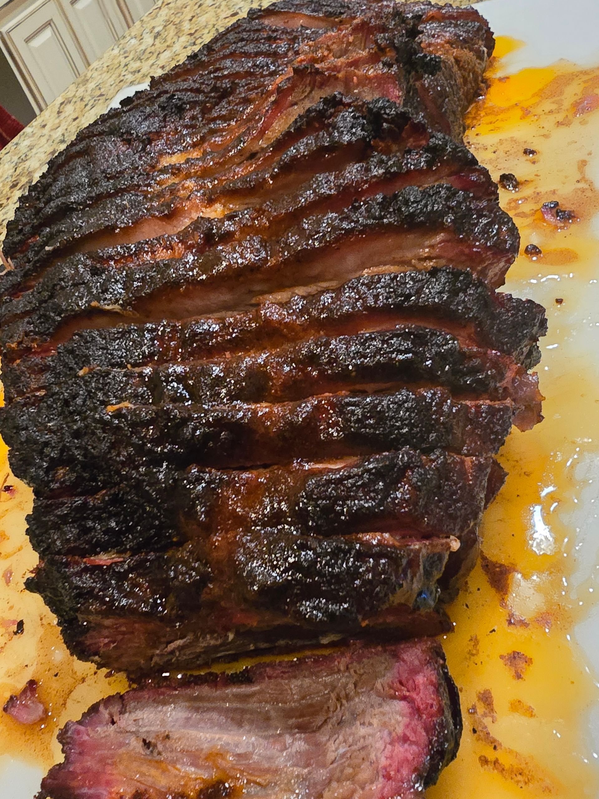 Sliced smoked brisket on a white plate, dark bark, reddish-pink interior, surrounded by rendered fat.
