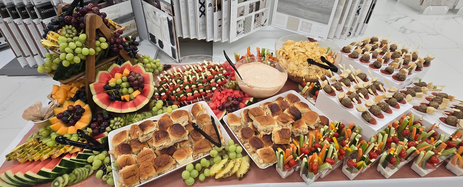 Buffet spread with fruit basket, sandwiches, and small tacos.