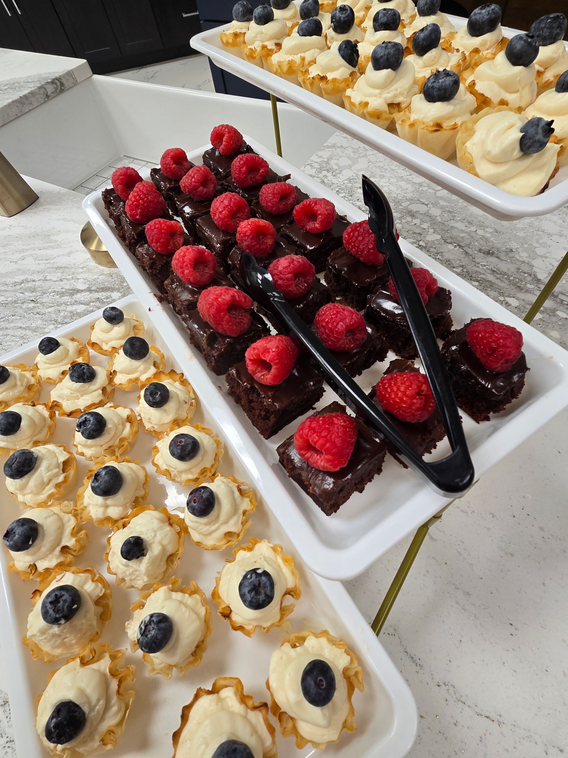 Dessert tray with mini tarts, brownies with raspberries, and blueberry pastries.