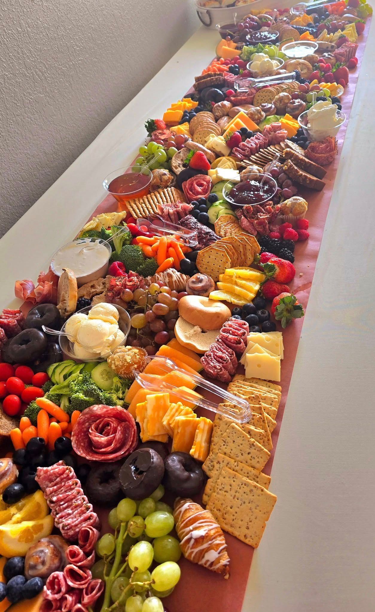 Long charcuterie board with various cheeses, meats, fruits, crackers, and vegetables arranged on a red runner.