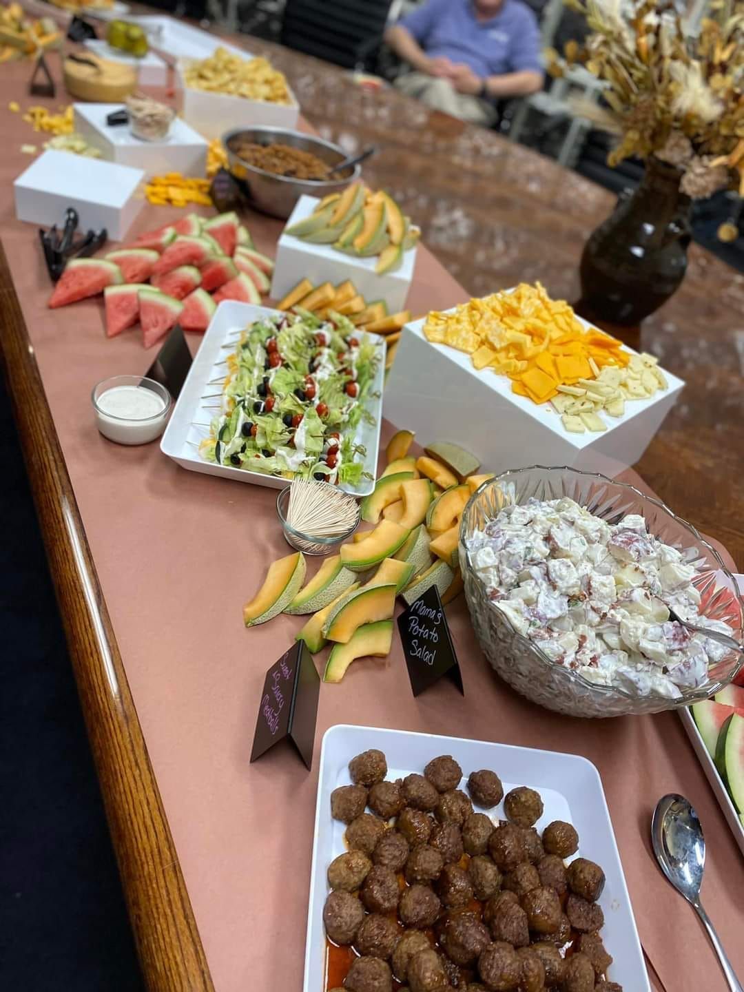 Long table laden with food: cheese, fruit, salads, snacks, meatballs, and more. Someone in the background.