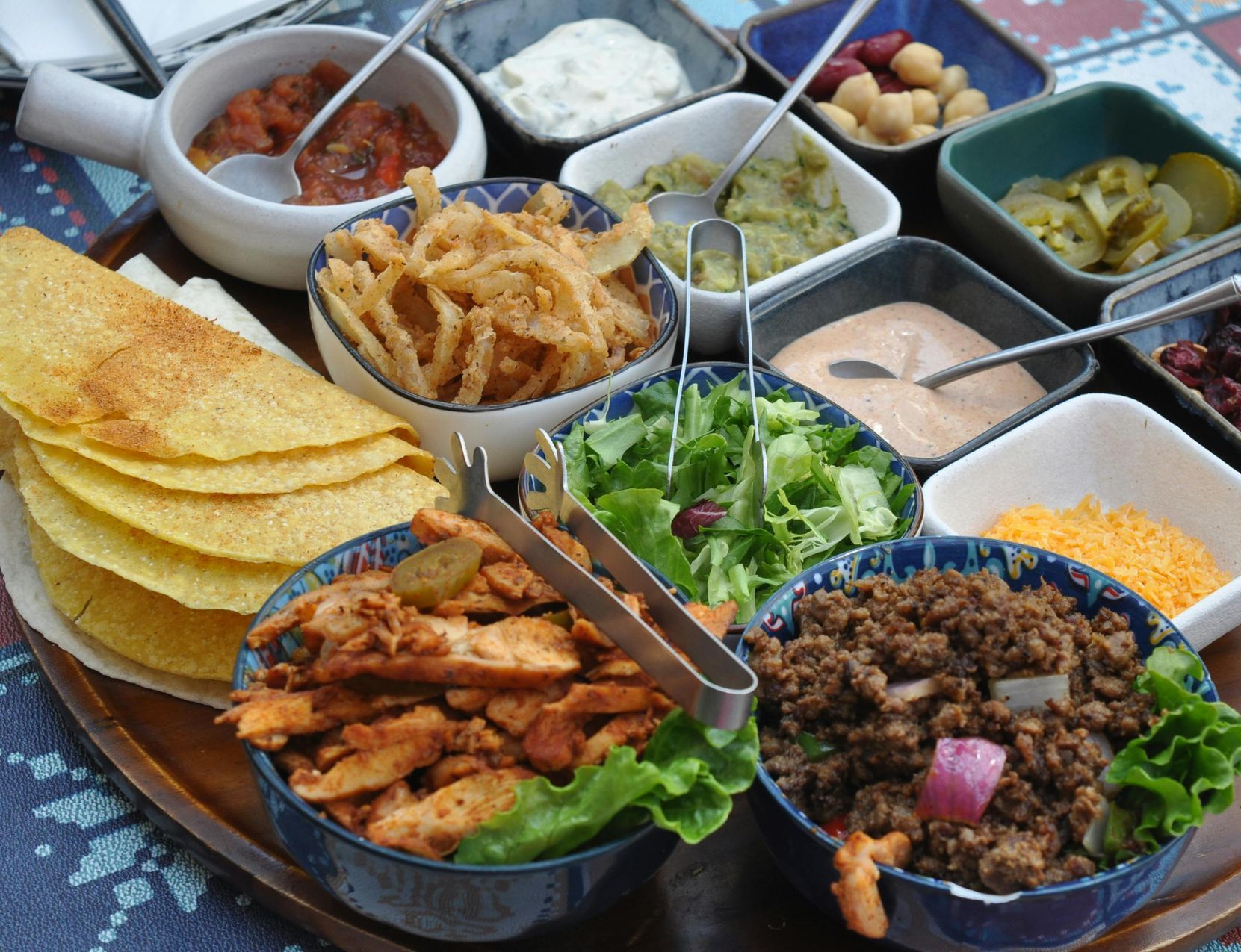 Taco bar with various fillings, including meat, veggies, and toppings, served in individual bowls.