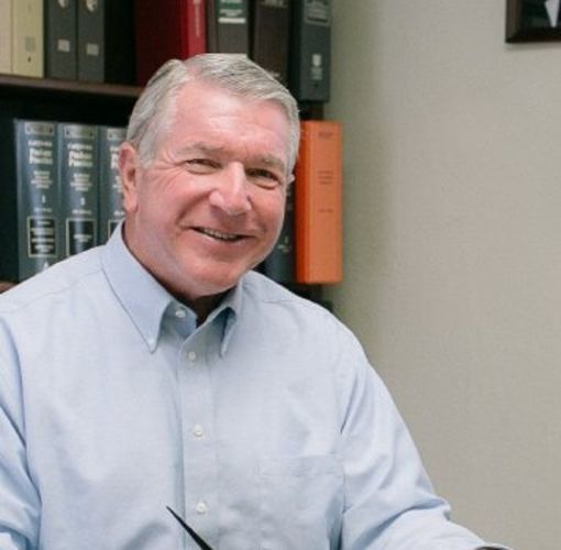 A man in a blue shirt is smiling in front of a shelf of books
