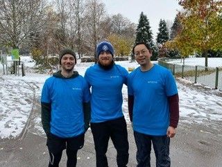 Three people in blue shirts stand in a snowy park.