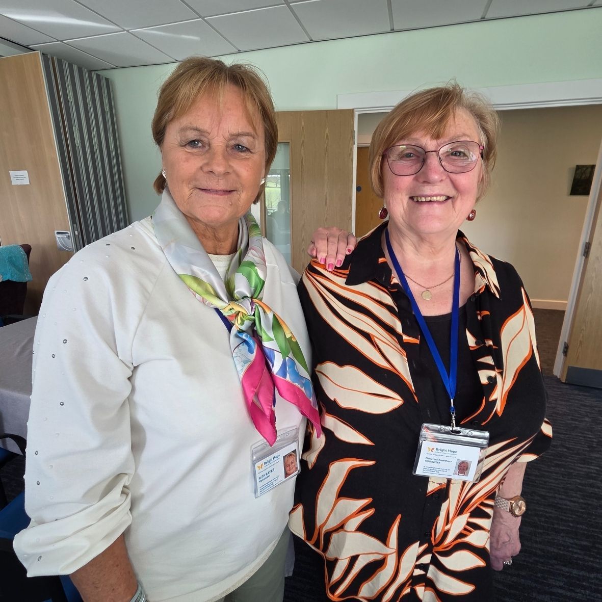 Woman smiles at an elderly person seated in a chair, a walker nearby.