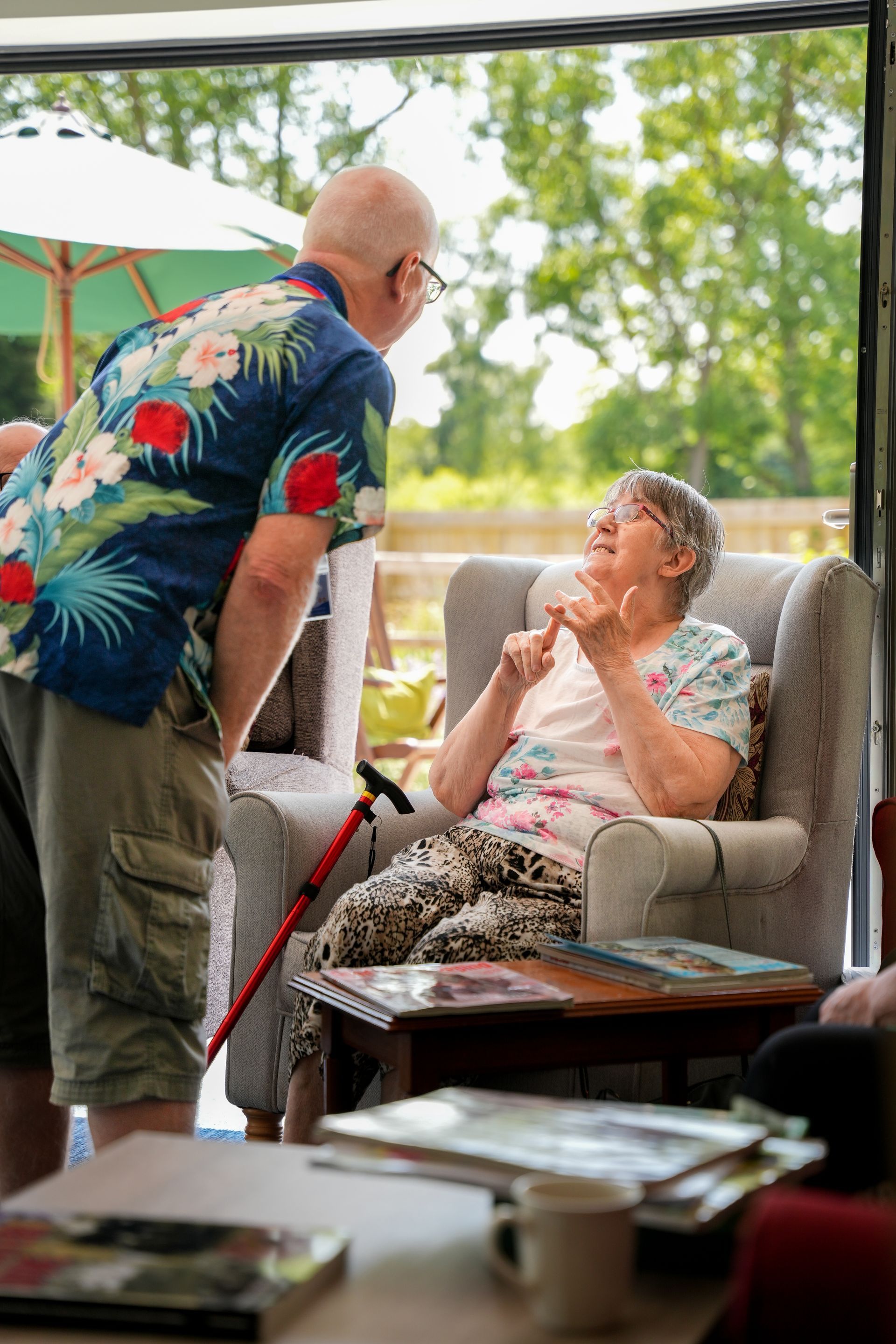 Man in floral shirt talking to a woman seated in a chair, gesturing with her fingers.