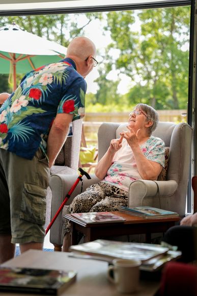 Man in floral shirt talking to a woman seated in a chair, gesturing with her fingers.