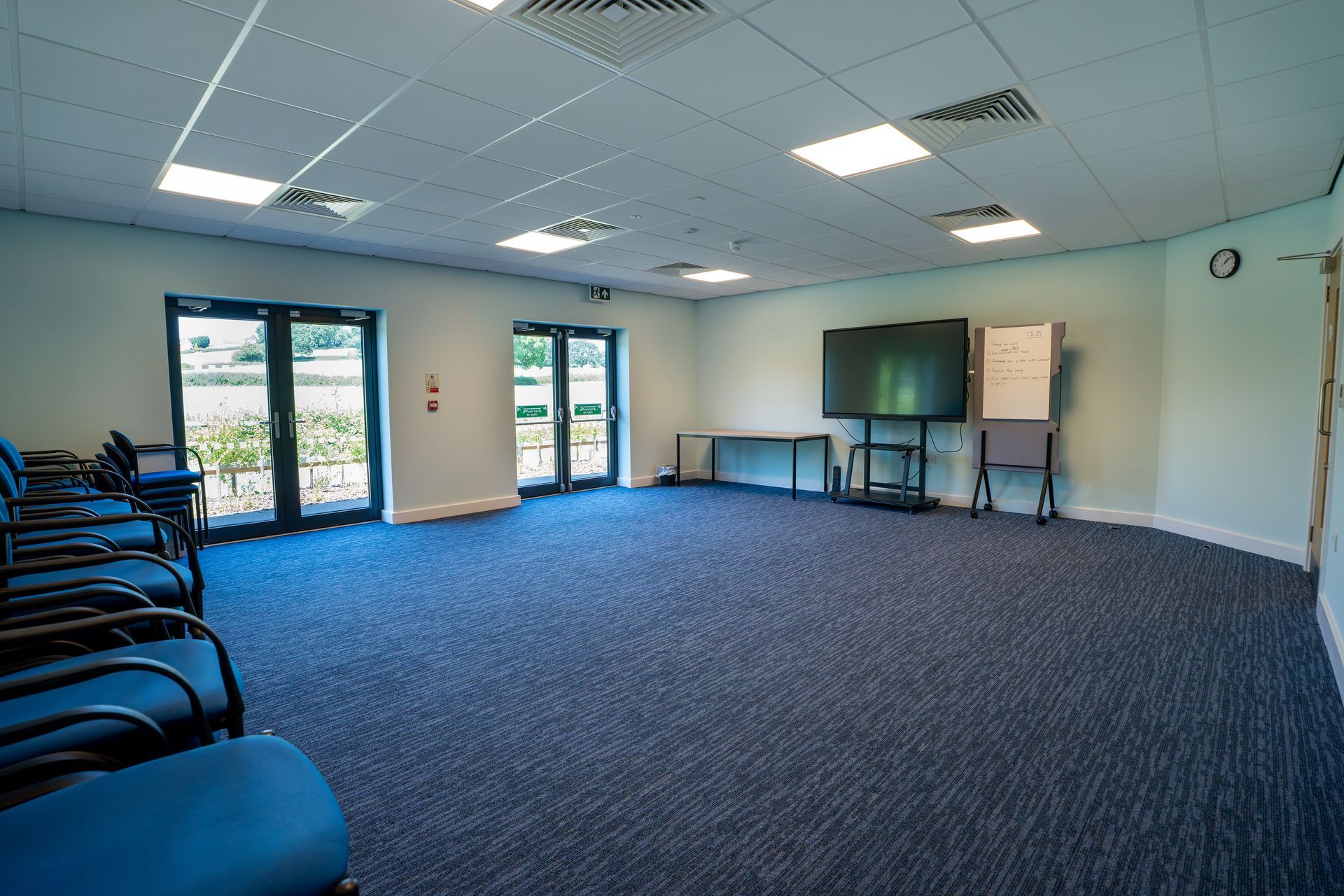 Empty conference room with blue carpet, rows of chairs, and a large screen.