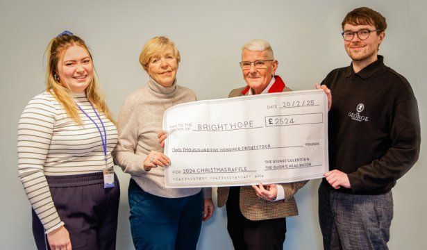 Four people holding a large check indoors, smiling.