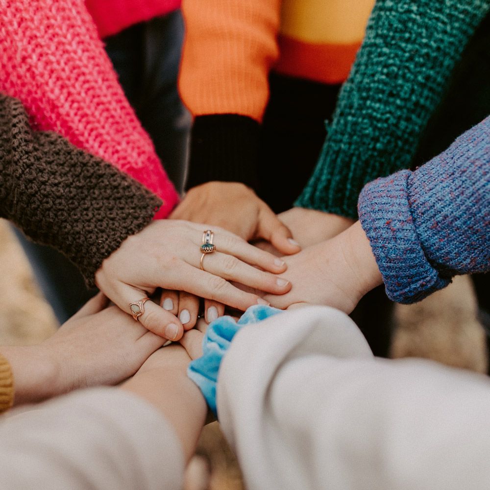 Hands stacked together, wearing colorful sweaters.