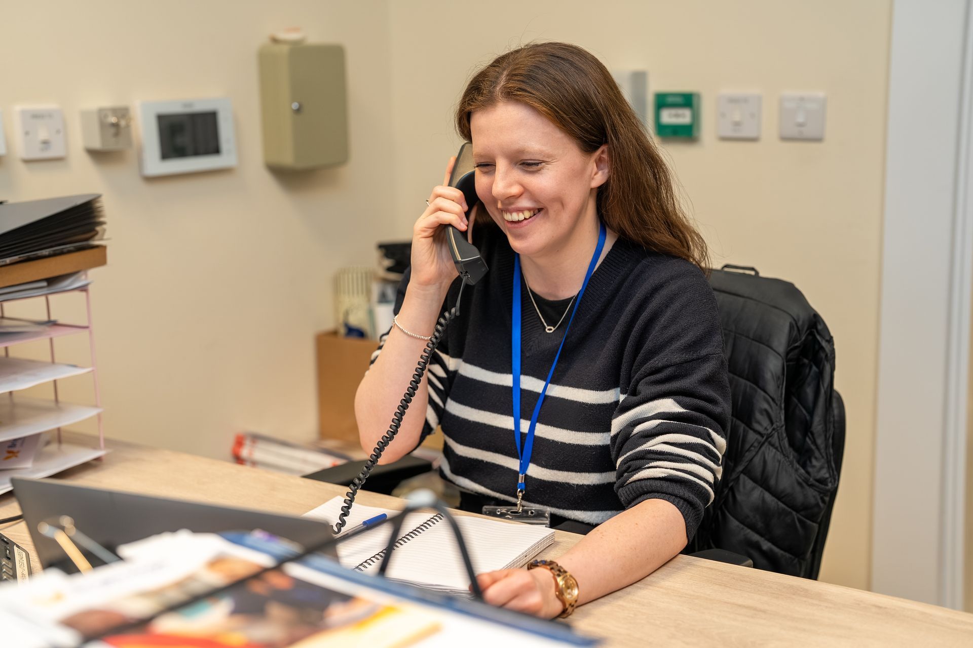 Woman at a Bright Hope reception desk, smiling. Yellow banner promoting volunteering; donation jar visible.