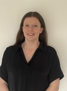 Woman in black shirt smiling at the camera, standing in front of a white wall.