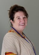Woman smiling, wearing a light-colored sweater and a lanyard, in front of a neutral background.