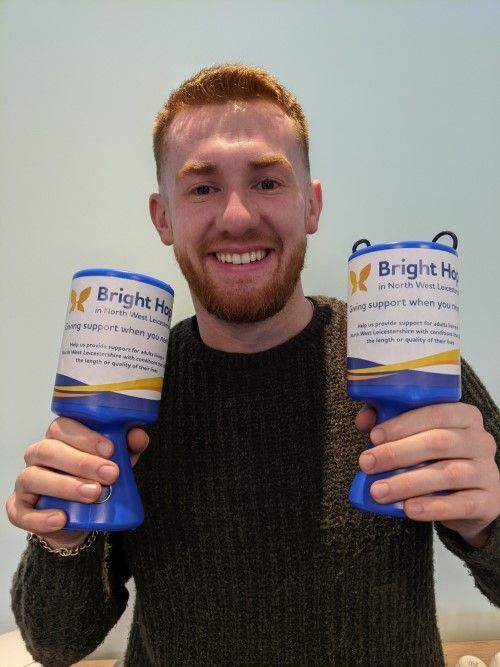 Man smiling, holding two blue and white donation collection jars.