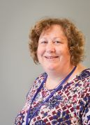 Woman with curly brown hair smiles, wearing patterned top and lanyard.