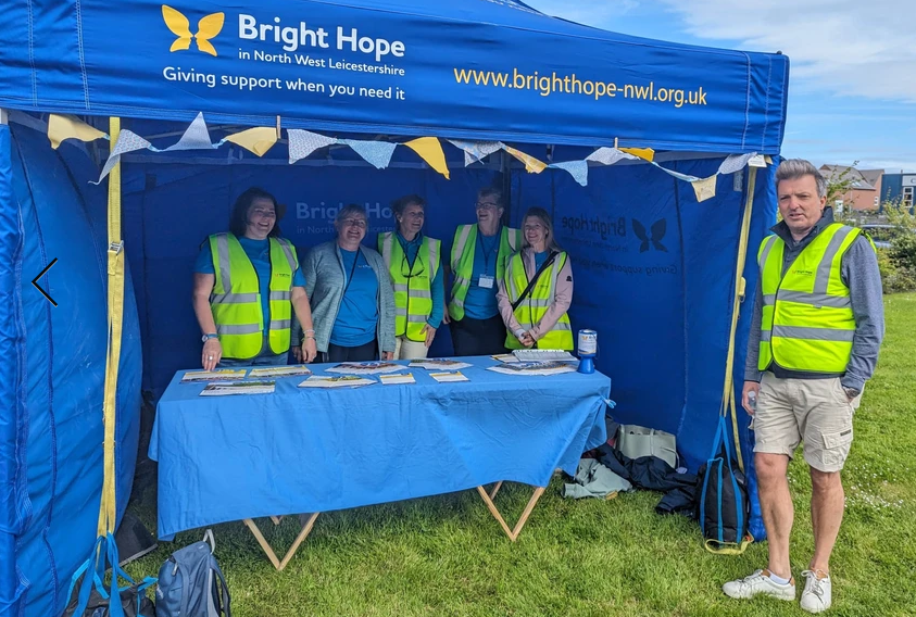 People at a blue Bright Hope charity tent, all wearing yellow vests.