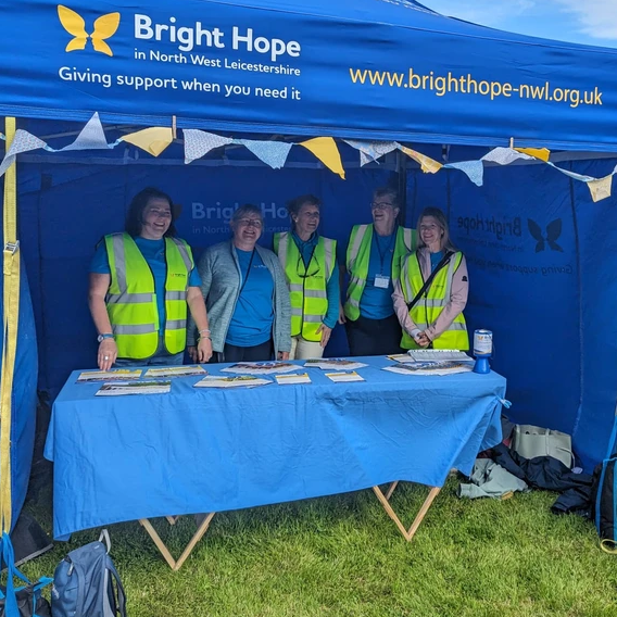 Bright Hope booth at an event. Five people wearing vests stand behind a blue table with pamphlets.