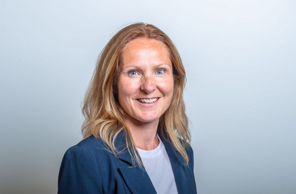Woman with blonde hair, wearing a blue blazer and white shirt, smiles at the camera.