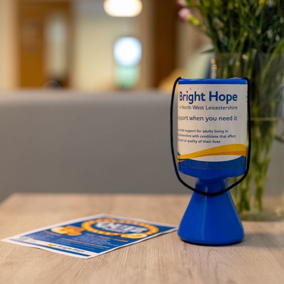 Woman smiles at an elderly person seated in a chair, a walker nearby.